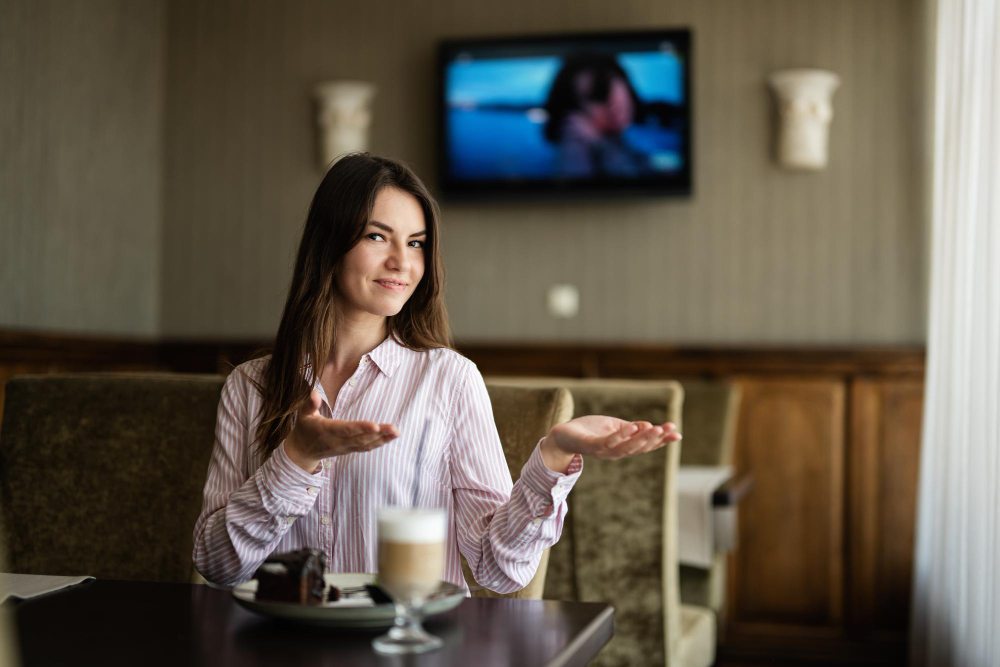 zena u kaficu a iza ledja na zidu veliki televizor